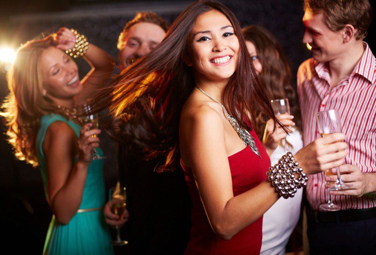 Portrait of cheerful girl with champagne dancing at party and smiling at camera